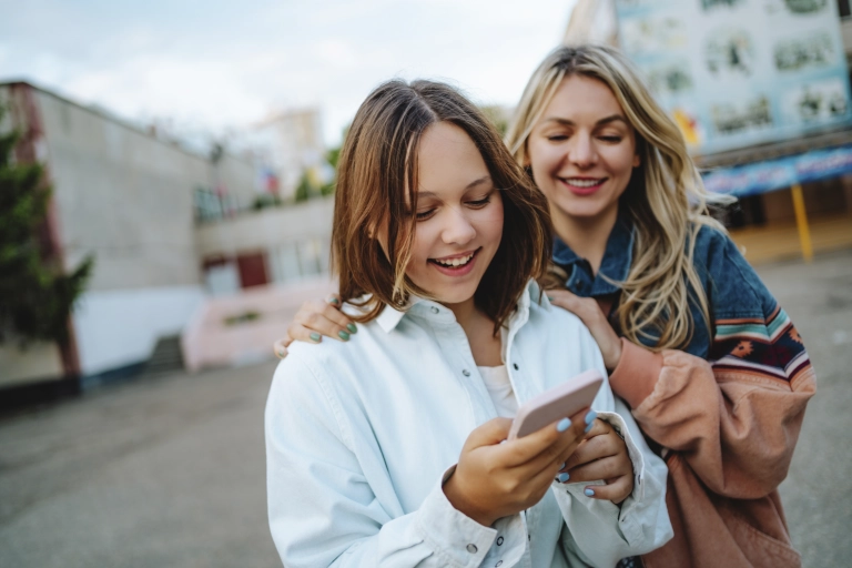 zwei junge Mädchen schauen auf ein Handy und lächeln