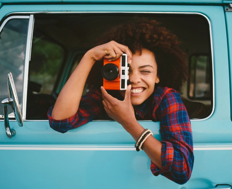 eine junge FRau in Karobluse fotografiert aus einem Autofenster heraus und lacht